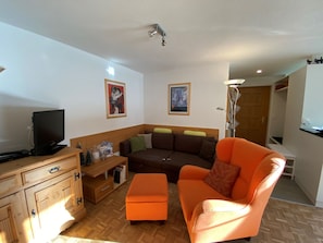 Ein Wohnzimmer mit einer Couch, einem Hocker, einer Holzkommode und einem Fernseher.