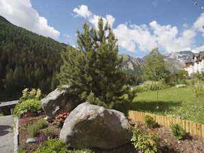 A mountainous landscape with a house surrounded by a garden with large rocks and flowering plants.