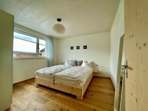 Ein Schlafzimmer mit einem Holzbett, einem Fenster mit Vorhängen und einer Wandleuchte.