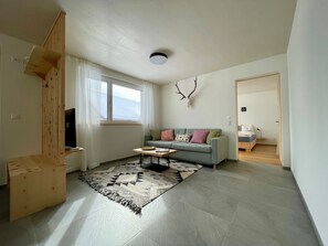 Een moderne woonkamer met een grijze bank, een houten salontafel en een vloerkleed met dessin.