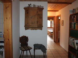 Un mueble de madera con tapa metálica, una silla y una estantería en una habitación con vigas de madera y suelo de baldosas.