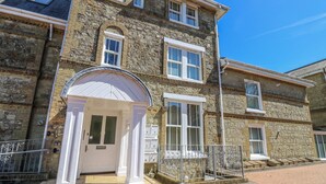 A stone building with a gated entrance, multiple windows, and a small covered area with a door. - 6 Priory (Shanklin)