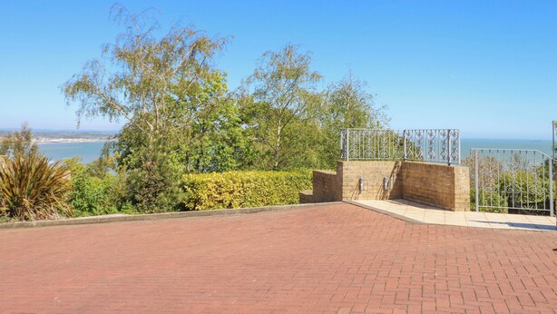 A paved outdoor area with a brick floor, surrounded by greenery and a view of the sea. - 6 Priory (Shanklin)