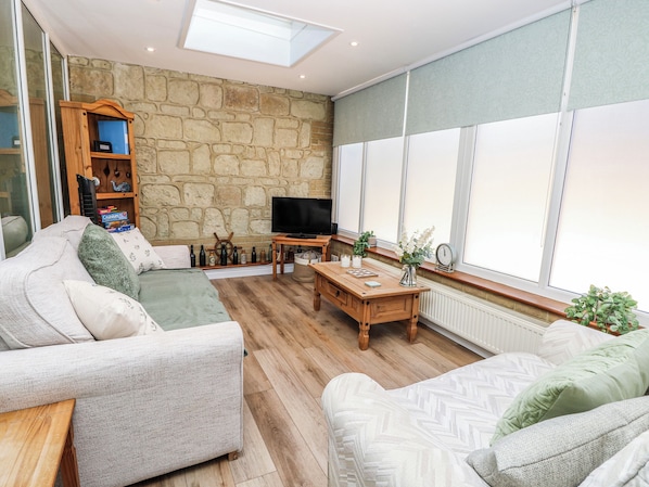 Una sala de estar con pared de piedra, televisor, mesa de centro de madera y sofá.