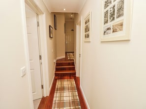 A hallway with a wooden staircase, a checkered carpet, and framed pictures on the walls. - 6 Priory (Shanklin)