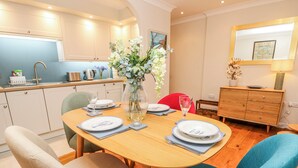 A dining area with a wooden table, chairs, and a vase with flowers. - 6 Priory (Shanklin)