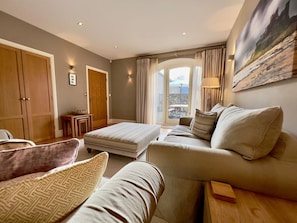 A room with a sofa, ottoman, wooden cabinet, and a painting on the wall. - The Chimney (Bamburgh)