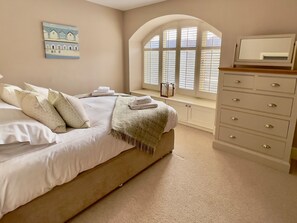 A bedroom with a bed, a dresser, a window with blinds, a painting on the wall, and a bench by the window. - The Chimney (Bamburgh)
