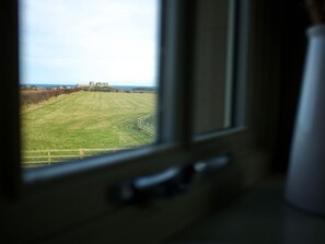 A view through a window of a grassy field with a distant building, possibly a castle, and a clear sky. - The Chimney (Bamburgh)