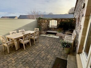 A patio with a table and chairs, a stone wall, a bench, and a potted plant. - The Chimney (Bamburgh)