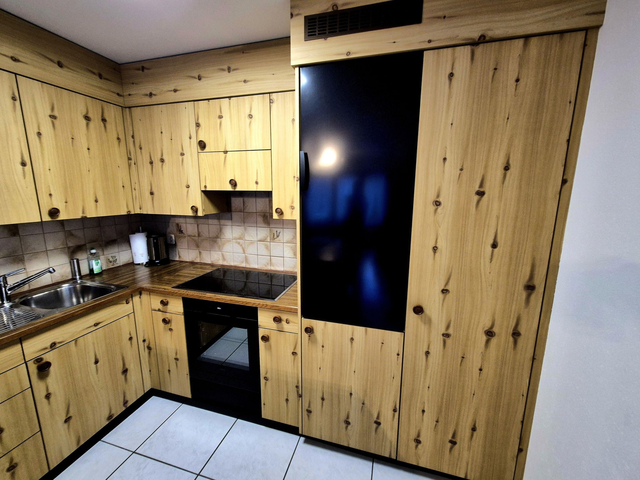 A kitchen with wooden cabinets, a black dishwasher, and a tiled backsplash.