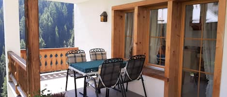 A balcony with a table and chairs, a wooden railing, and a view of a forest.
