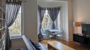 Ein modernes Wohnzimmer mit einer Couch, einem Esstisch mit Stühlen, einem Fernseher und einem Deckenventilator.