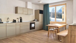 Een moderne keuken met inbouwapparatuur, een eethoek met een houten tafel en stoelen, en een groot raam met uitzicht op een besneeerd landschap.