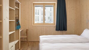 Een kamer met houten wanden, een bed, een raam met gordijnen, een stoel en een kledingkast.
