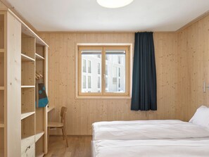 A room with wooden walls, a bed, a window with curtains, a chair, and a wardrobe. - Hotel Maistra 160, (Pontresina), by Interhome (Pontresina)