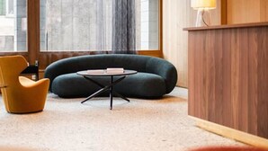 Een kamer met een bank, een stoel, een kleine tafel, een houten receptiebalie en een groot raam.