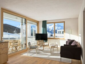 A modern living room with a large window, a flat-screen TV, wooden furniture, and a view of snow-capped mountains. - Hotel Maistra 160, (Pontresina), by Interhome (Pontresina)