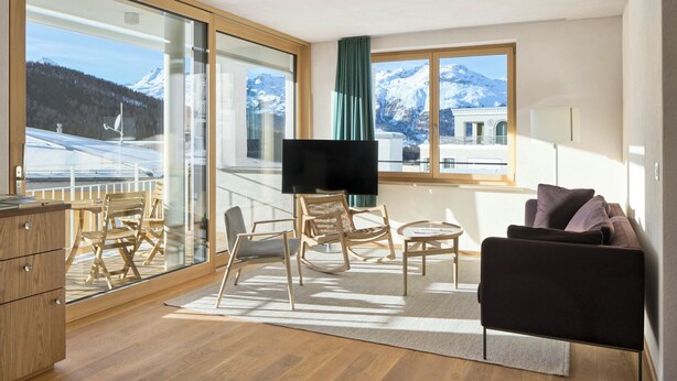 Een moderne kamer met een groot raam, een flatscreen televisie, houten meubilair en uitzicht op besneeuwde bergen.