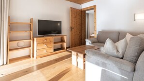 Ein modernes Wohnzimmer mit Holzboden, einem Flachbildfernseher auf einem Holzbodenständer, einem grauen Sofa und einem Couchtisch aus Holz.