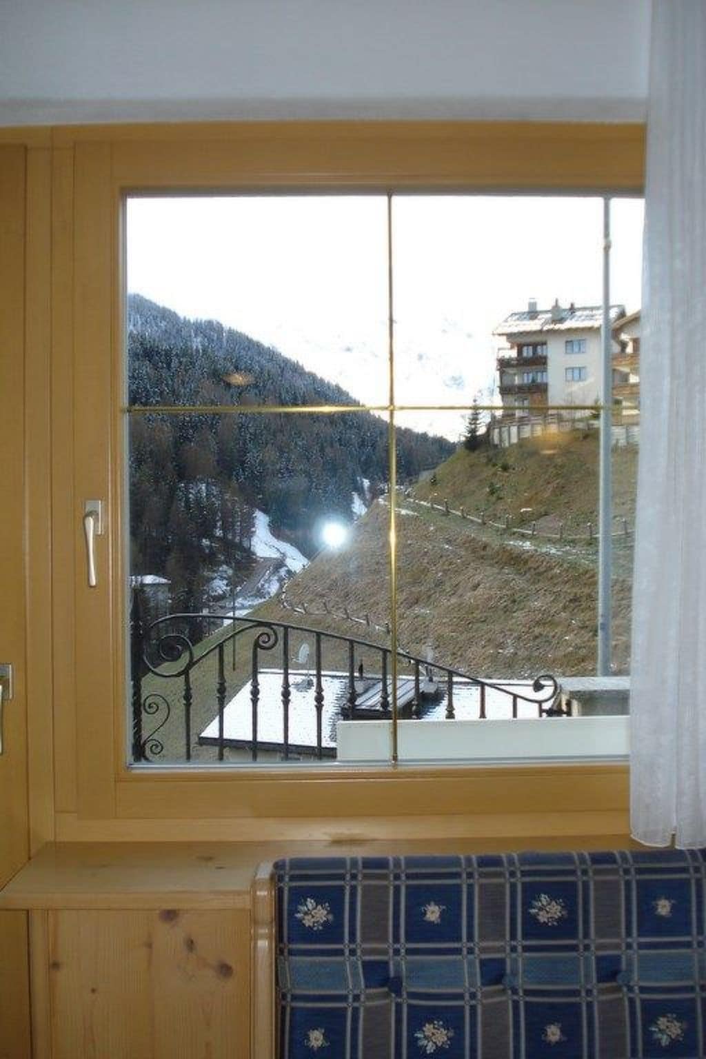 A room with a large window overlooking a mountainous landscape, a wooden door, and a blue patterned bench.