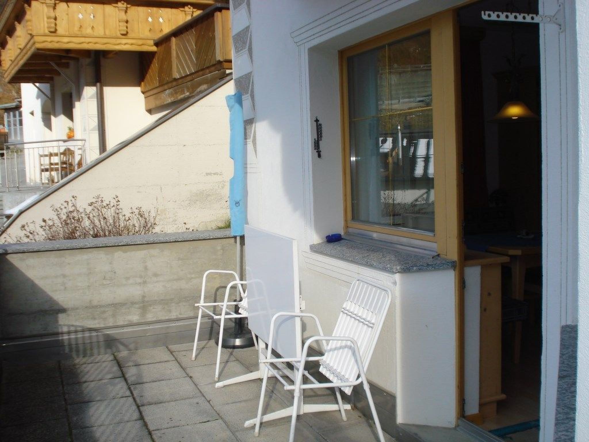 Un patio con dos sillas blancas, una ventana con vistas y una escalera de madera.