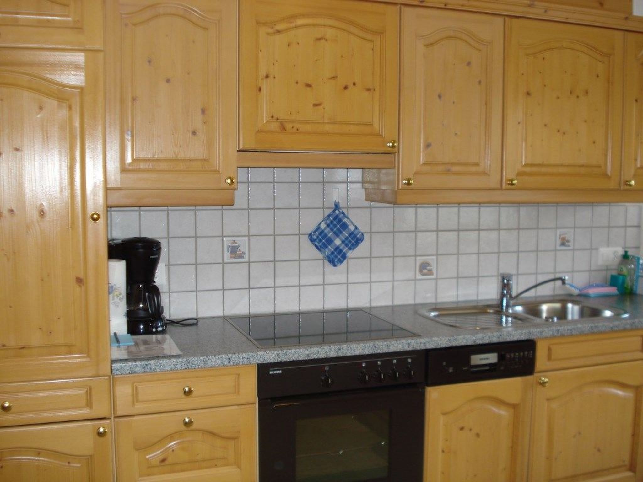 Cuina amb armaris de fusta, rentaplats, forn, cafetera i salabost a la paret.