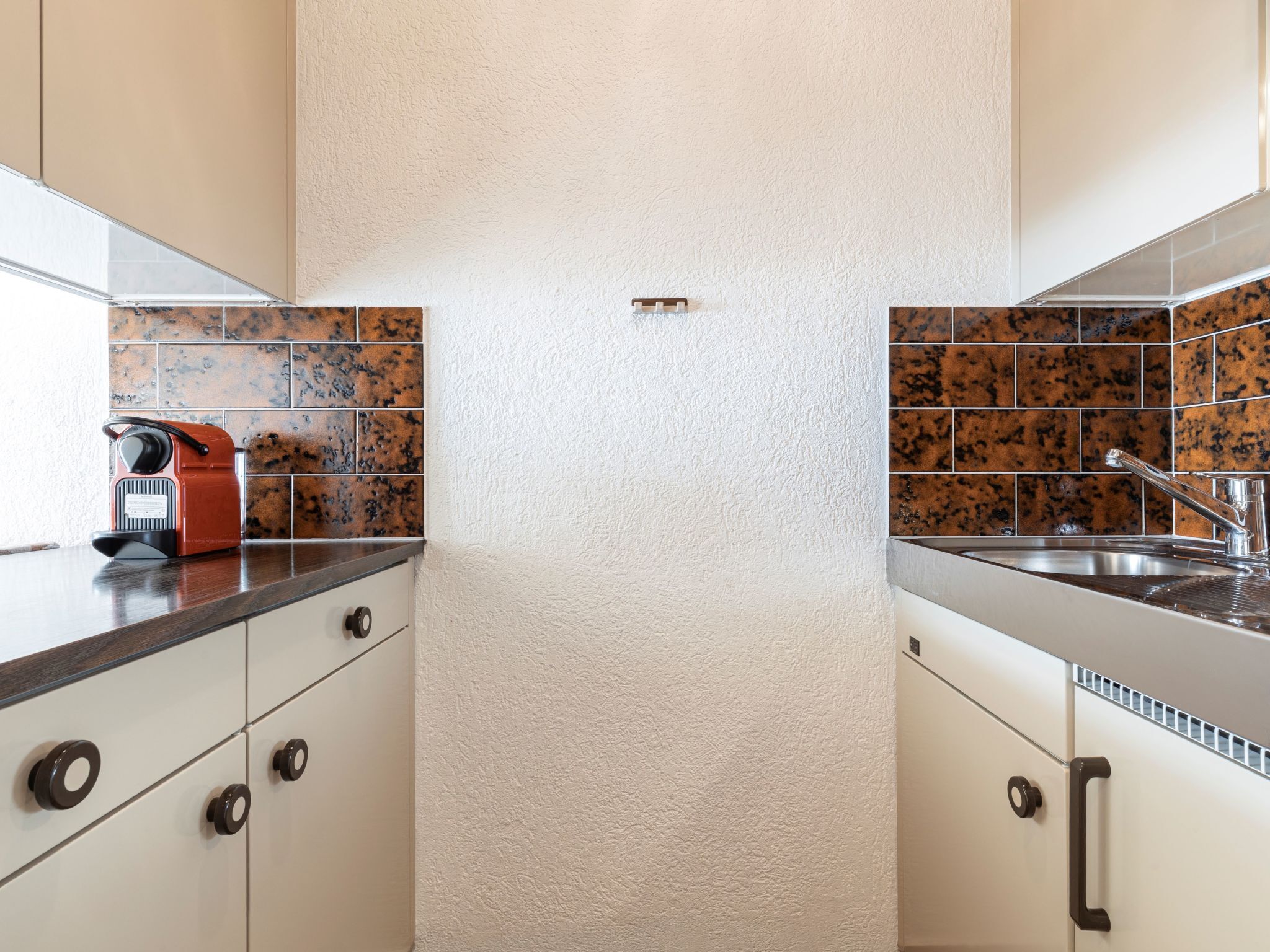 Une cuisine avec des meubles blancs, un appareil électroménager rouge et un pare-feu décoré de carreaux bruns.