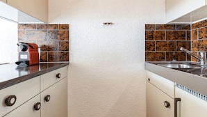 Cozinha com armários brancos, eletrodoméstico vermelho e painel atrás do fogão com azulejos marrons.
