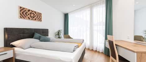 Un dormitorio moderno con cama, mesita de noche, escritorio, silla y un amplio ventanal con cortinas.