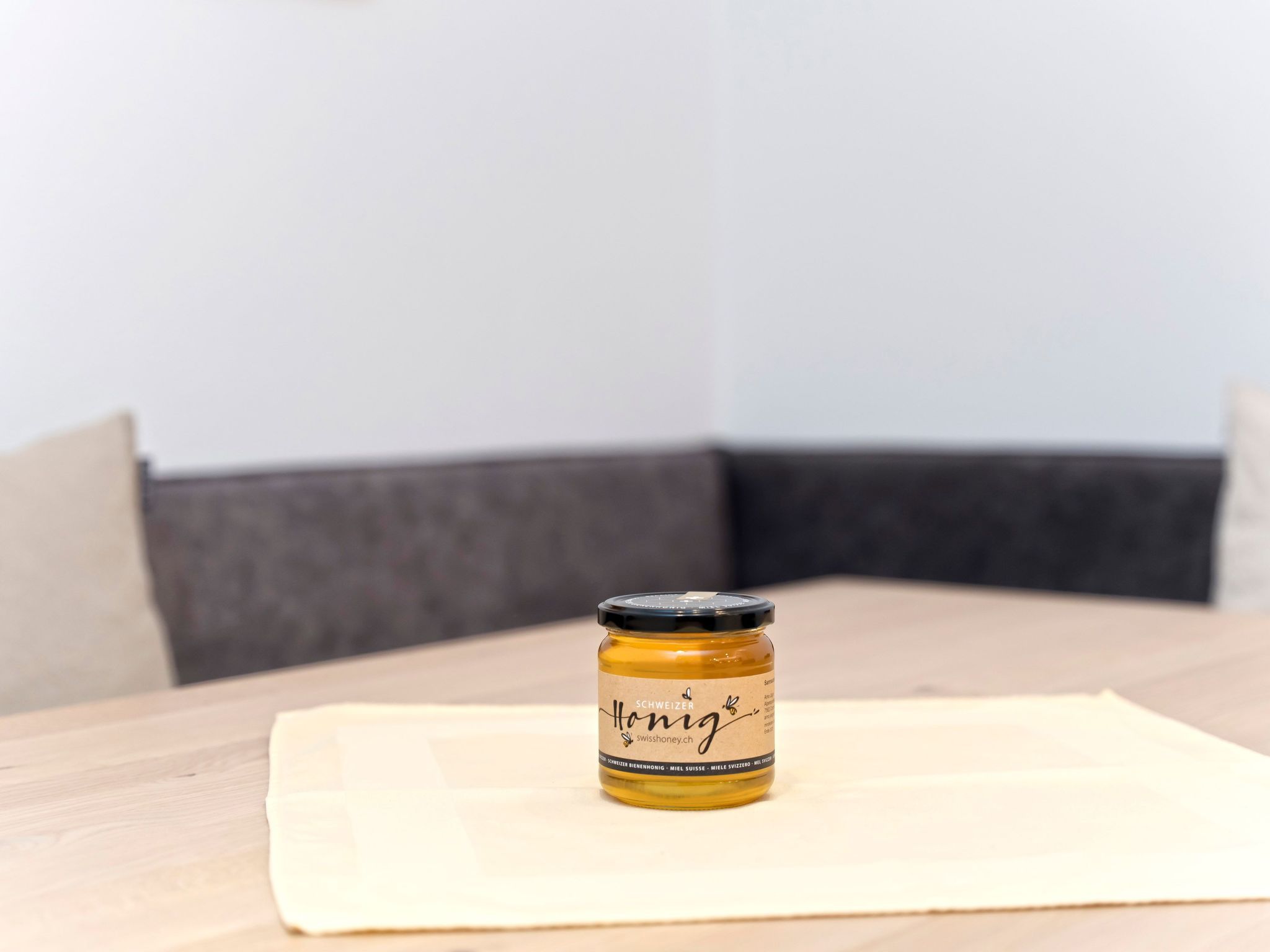 Un pot de miel sur une table en bois, avec un coussin en arrière-plan.
