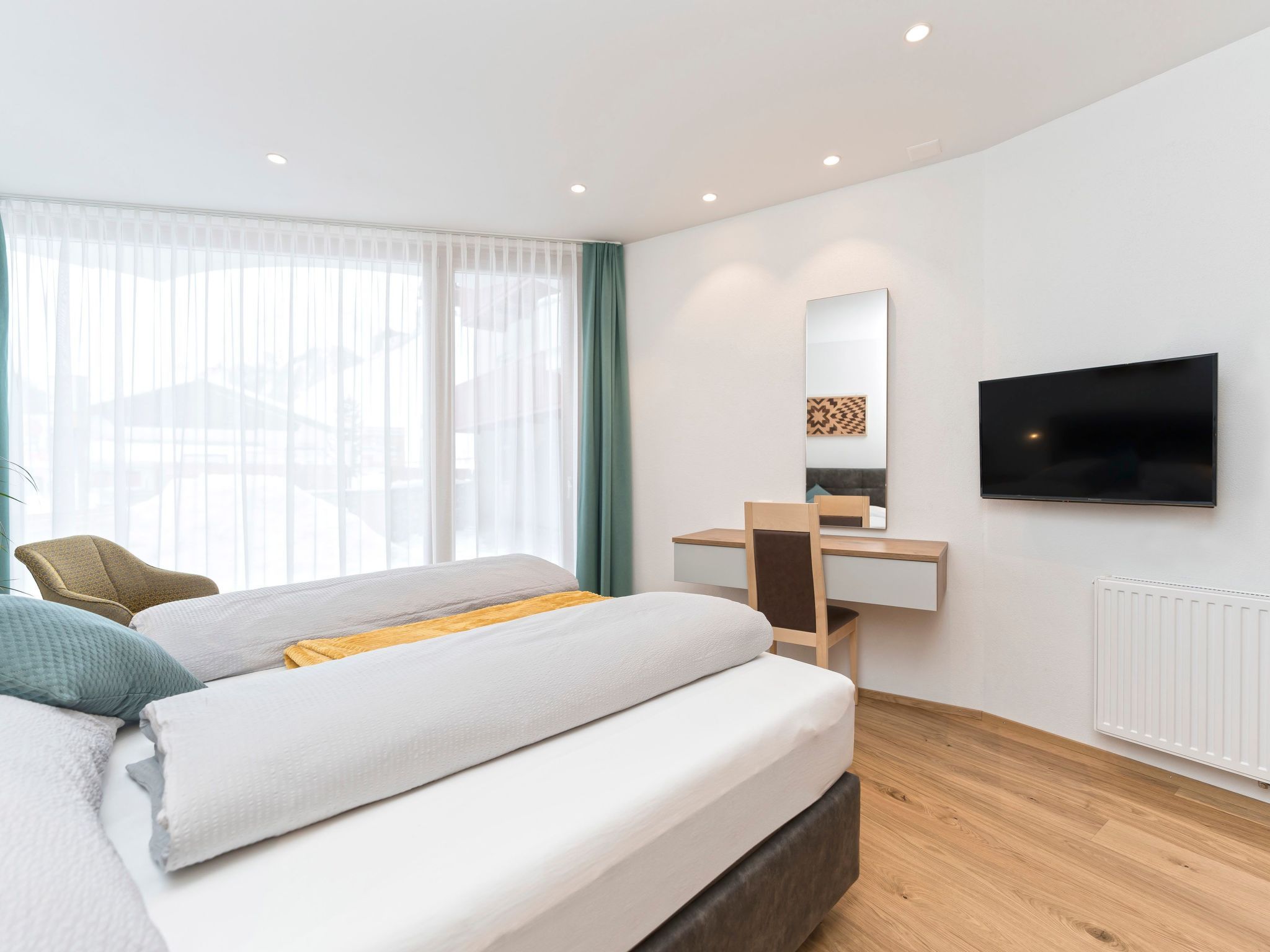 A modern bedroom with a bed, a desk, a chair, a television, and a window with curtains.