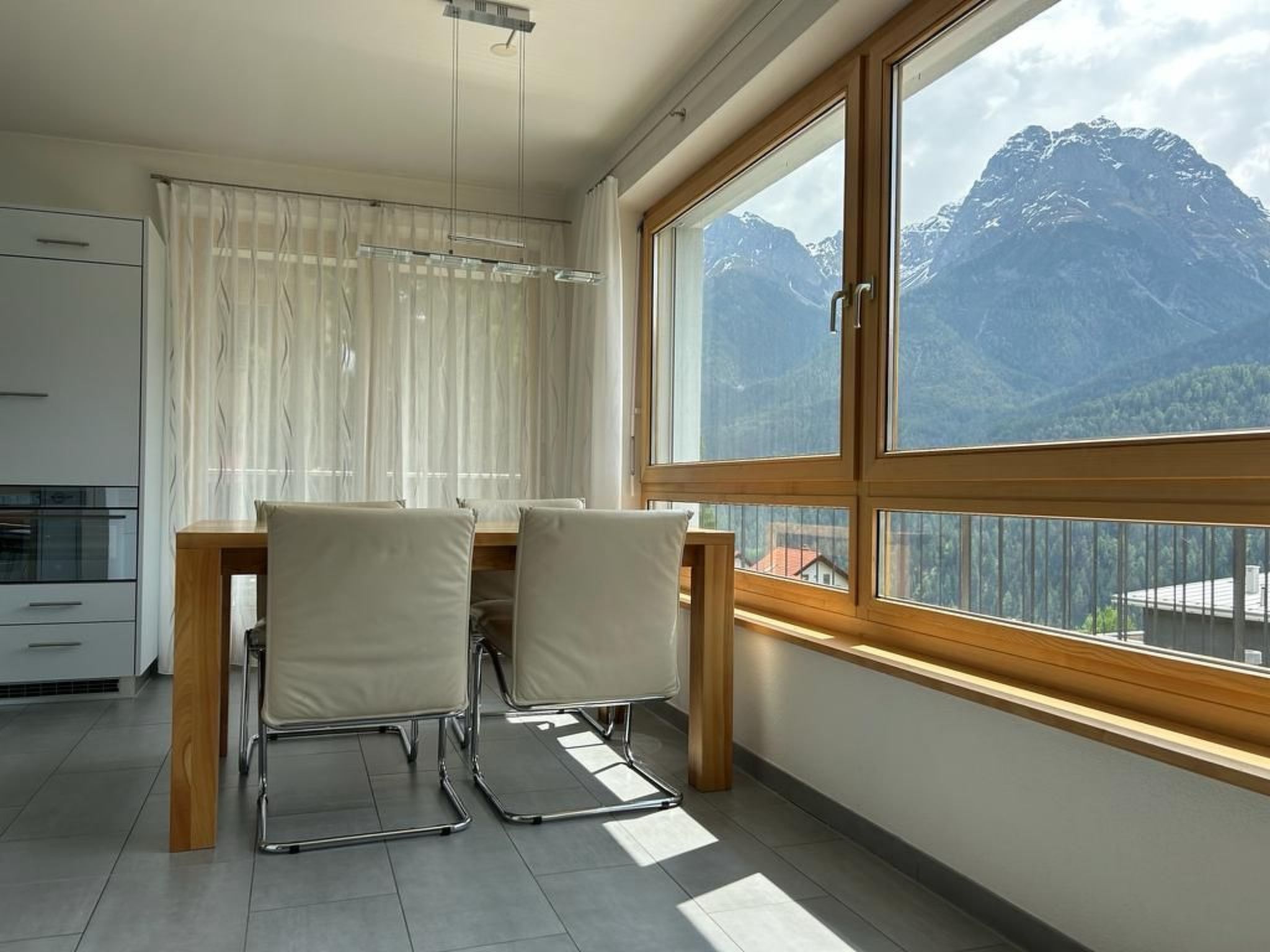 Une cuisine moderne avec un coin repas, une grande fenêtre donnant sur les montagnes et un luminaire au plafond.