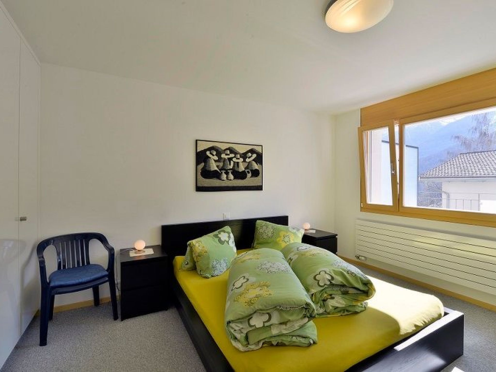 Une chambre à coucher comprenant un lit, une chaise, une table de chevet, un tableau accroché au mur et une fenêtre.