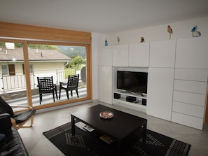 A modern living room with a large TV, black furniture, and a view of the outdoors. - SOTRACHÖGNA EG, (Scuol) by Interhome (Scuol)