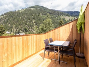 Eine Holzterrasse mit Tisch und Stühlen mit Blick auf einen bewaldeten Hang.