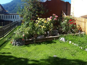 A garden with a variety of flowers, a wooden fence, and a building in the background.