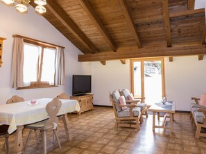 A room with a wooden ceiling, a television, a dining table with chairs, a sofa, and a window with curtains. - Mundaditschas, (Sta. Maria - Santa Maria Val Müstair) by Interhome (Sta. Maria GR)