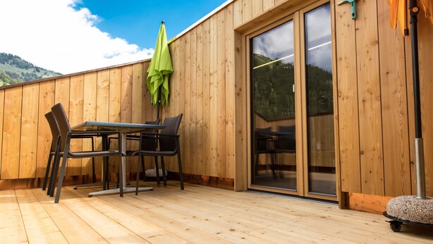 Eine Holzterrasse mit Tisch und Stühlen, einer Glasschiebetür und einem grünen Sonnenschirm.