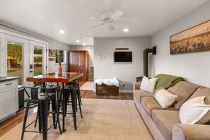 Eine moderne Küche mit Essbereich, einer Couch mit Kissen, einem Deckenventilator und einem an der Wand montierten Fernseher.