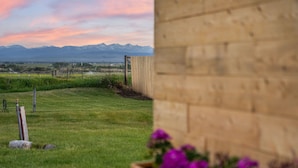 A grassy outdoor area with a wooden fence, a wooden structure, and a mountain range in the background.