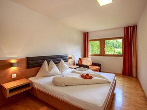 A hotel room with a large bed, a bedside table, a chair, a window with curtains, and a view of greenery outside. - Apart Lischana, (Samnaun-Laret) by Interhome (Samnaun)