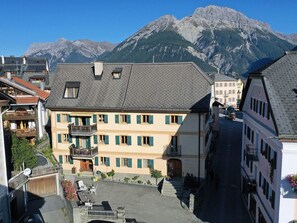 Ein Gebäude mit einem Balkon, eine Straße davor und Berge im Hintergrund.
