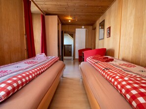 Ein Zimmer mit zwei Betten, Holzwänden, einer Holzbalkendecke und einem roten Stuhl.