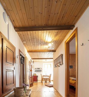 A hallway with wooden ceiling beams, a wooden door, a wall-mounted light fixture, and a bed with a wooden headboard. - Ferienwohnungen Chasa Werro, (Sent) by Interhome (Sent)