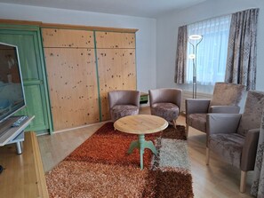 Ein Wohnzimmer mit einer Sofagarnitur, einem Couchtisch, einem Fernseher und einem Kleiderschrank.