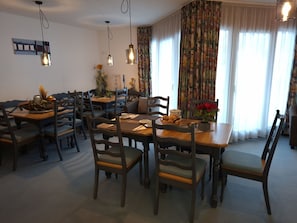 Ein Essbereich mit Holztischen und -stühlen, einer Kaffeestation und Blick ins Freie durch große Fenster.