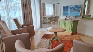 Una sala de estar con un conjunto de sofás, una mesa de comedor con sillas, un televisor y un aparador verde.