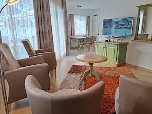 Ein Wohnzimmer mit einer Sofagarnitur, einem Esstisch mit Stühlen, einem Fernseher und einem grünen Schrank.