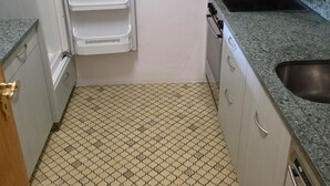Uma cozinha compacta com armários brancos, bancada de granito e piso estampado.